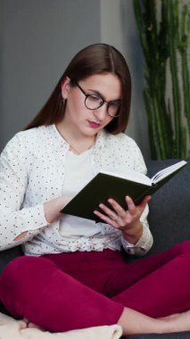 Genç öğrencinin kitap okuduğu dikey format videosu. Evdeki yatakta kitap okuyan güzel, genç esmer kadın..