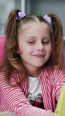 Dikey Kız Videosu tablet üzerinde bir oyun oynuyor ve kameraya bakıyor. Küçük kız dijital tablet teknolojisi kullanıyor. Evde kucak dolusu bilgisayar oyunu oynanıyor. Çocuklar teknoloji bağımlılığı