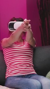 VR kulaklıkla oynayan ve gülümseyen genç bir kadının dikey format videosu. Renkli ışıklandırma arka planında sanal gerçeklik miğferi