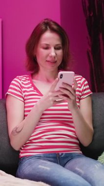 Mutlu Rahat Genç Kadın 'ın Akıllı Telefon Bakışlı Ekran Gülen Mobil Uygulamaları Kullanmaktan Keyif Alırken Ev Sahipleri Kanepesinde Sosyal Medya Sohbeti' nin dikey Format Videosu