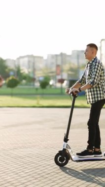 Elektrikli scooterla işe gidip gelen bir adamın dikey videosu. Çevre dostu ulaşım. Hızlı sürüşlü elektrikli taşıma. Escooter süren bir adam. Ekoloji ve kentsel yaşam tarzı.