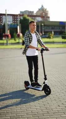 Modern ulaşım elektrikli scooter 'ıyla işe giden tişörtlü genç adamın dikey videosu. Sabahları sokakta scooter 'la gezen bir iş adamı. Ekoloji ve kentsel yaşam tarzı.