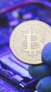 İş adamının dikey format videosu anakart arka planında altın Bitcoin tutuyor. Parmaklarda kripto para. İnsan gelecekteki para birimini gösteriyor. Madencilik, ticaret.