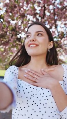 Şehir parkında akıllı telefondan gülümseyen bir kızın video görüntüsü, kameraya el sallayan arkadaş canlısı bir kadın, telefonda konuşan güzel bir kadın, dışarıda telefonla video çeken şık bir blogcu..