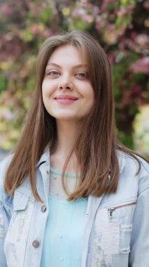 Sokakta kameraya bakan gülümseyen genç bir kadının dikey formatı. Mutlu kız portresi. Güzel, modern bir kadın.