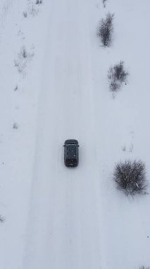 Kış karında bir araba yolunun havadan görünüşünü gösteren dikey format videosu. Kış yolunda uçuyor. Karla kaplı bir yolda araba sürüyor. Karlı bir yolda yarış arabası sürmek.