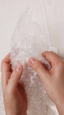 Kadının dikey format videosu bir baloncuk ambalajına basar. Beyaz arka planda baloncuklu ambalajda kadın elleri hava kabarcıkları patlatıyor. Sinir sistemi konseptini sakinleştirmek