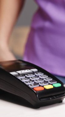 Mağaza çalışanının elinde Pos-terminal 'in dikey videosu. Elektronik ödeme makinesinden ya da kart okuyucudan cep telefonuyla satın alma. Oteldeki kadın müşterinin nakitsiz cüzdanında e-para.