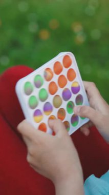 Popit 'le oynayan stresli kişinin dikey format videosu pop baloncuğu oyuncağını itiyor. Popüler bir anti-stres oyuncağı oyunu oynamanın zirvesi. Çocukların elleri gökkuşağı oyuncağıyla oynar..