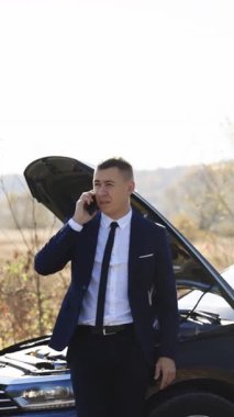 Yoldaki araba kazasının dikey format videosu. Elektrikli arabasının bozulduğunu söyleyen bir adam aradı. Acil dur işareti. Beyaz adam telefonla konuşuyor. Araba servisine yardım etmesi için birini arıyor.