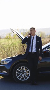 Yoldaki araba kazasının dikey format videosu. Elektrikli arabasının bozulduğunu söyleyen bir adam aradı. Acil dur işareti. Beyaz adam telefonla konuşuyor. Araba servisine yardım etmesi için birini arıyor.