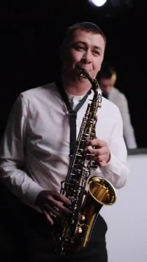 Saksafoncu Play 'in Altın Saksafon' daki dikey format videosu. Havalı saksafoncu sahnede solo performans sergiliyor. Grupta müzisyen çalıyor. Canlı performans. Caz müziği.