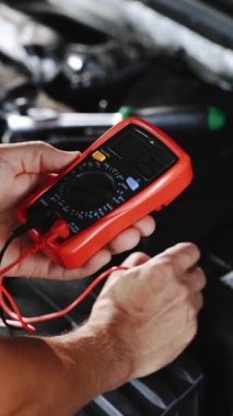 Elektrikli çoklu sayaçlı batarya voltajının dikey format videosu. Araba marş pili. Profesyonel tamirci araba servisinde çalışıyor. İyi, elektrikçi, elektrik, pil tam şarj