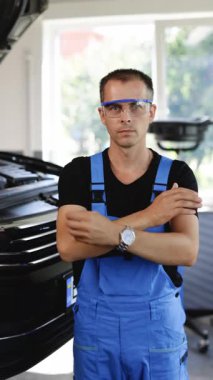 Yakışıklı Profesyonel Araba Tamircisinin Dikey Format Görüntü Portresi Bir Hizmette Bir Araç Üzerinde Çalışıyor. Tamirci güvenlik gözlüğü takıyor. Kameraya bakıyor..