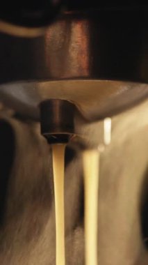 Kahve makinesinde bir fincan koyu kahve yapmanın dikey videosu, arka ışık buharı aydınlatıyor. Profesyonel makineden fincana kahve dökülüyor. Duble espresso yapıyorum..
