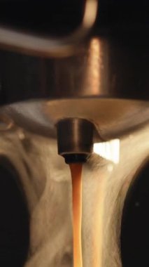 Profesyonel makineden kahve dökülürken çekilmiş dikey bir video. Duble espresso yapıyorum. Taze kahve akıyor. Sabahları kavrulmuş sade kahve içmek. Sıcak Kahve İçeceği Konsepti.
