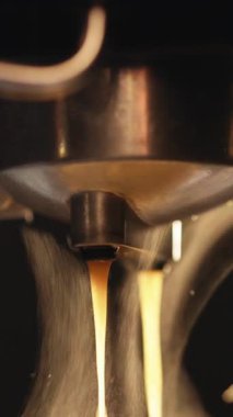 Kahve makinesindeki koyu kahvenin dikey videosu, arka ışık buharı aydınlatıyor. Profesyonel makineden fincana kahve dökülüyor. Espresso yapıyorum. Taze taze kahve..