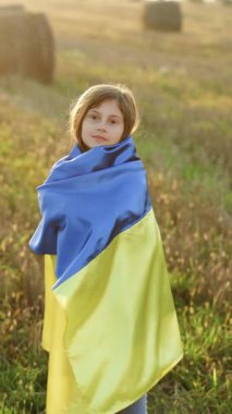 Ukrayna bayrağının mavi ve sarı bayrağını takan çocuk gülümsemelerini gösteren dikey video günbatımı arka planında dalgalanıyor. Ukrayna bayrağı mutlu Ukraynalı kızın ellerinde. Bayrak Günü. Anayasa Günü.