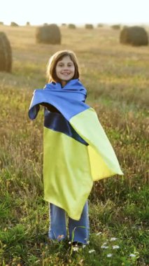 Mavi-sarı bayrak taşıyan Ukraynalı kızın dikey videosu. Ukrayna 'da savaş. Ukrayna Bağımsızlık Günü. Ukraynalı bir kızın portresi Ukrayna bayrağıyla günbatımına karşı tarlanın ortasında duruyor.