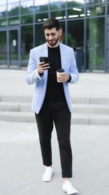 Muhteşem sakallı iş adamının finans bölgesinde cep telefonu kullanarak mesaj attığı dikey format videosu, cep telefonu mesajlaşması sırasında başarılı erkek CEO 'nun gülümsemesi.