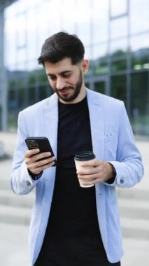 Modern şehirde sokakta yürürken cep telefonuna bakan mutlu Ermeni genç beyaz sakallı iş adamının dikey format videosu. Başarılı bir iş adamı işe gidiyor..