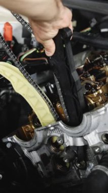 Araba tamircisinin araba servisindeki motoru tamir ederken çekilmiş dikey videosu. Tamirci, araç kullanarak otomobil motoru tamir ediyor. Otomobil ustası araçtan motoru tamir ediyor. Garajda ya da atölyede çalışan tamirci.