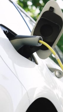 Elektrikli arabanın dikey format videosu. Çevre dostu elektrikli araba şarj ediliyor. Yeşil arka planda yüklenen araba. Araçlar yenilenebilir enerji kullanıyor..