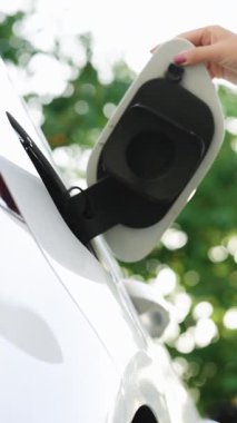 Kadının elinin dikey görüntüsü yeşil arka planda elektrik veya EV vagonu şarj etmek için güç kablosu sağlar. Elektrikli araba ya da elektrik şarj istasyonunda EV fişi takan kadın.