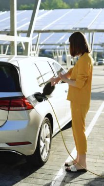 Elektrikli araba kablosunu söken kadının dikey format videosu. Kız akıllı saat üzerinde uygulama kullanarak şarj etmeyi durdurdu. Çevre dostu nakliye aracı. Kadın elektrik kablosunu koparıp elektrikli arabayı şarj ediyor..