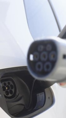 Kadınların el bağlantısını kestiği dikey video ve DC 'nin hızlı şarj olan soketini gösteriyor. Elektrikli araba fişi tutan bir iş kadını. Ev elektrik şarj istasyonunda elektrikli araba ya da EV takan bir kadın..