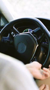 Sokak yolunda modern elektrikli araba kullanırken direksiyonu tutan tanınmayan kişilerin dikey format videosu. Pahalı araba kullanan kendine güvenen bir adam. Sürücü Dönen Direksiyon