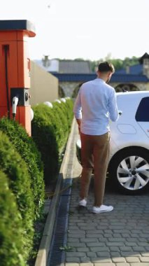 Elektrikli arabaları şarj eden tanımlanamayan bir adamın dikey format videosu. Sunbae elektrik kablosunu elektrikli bir arabaya takıyor. İş adamı şarj istasyonunda elektrikli arabayı şarj ediyor.