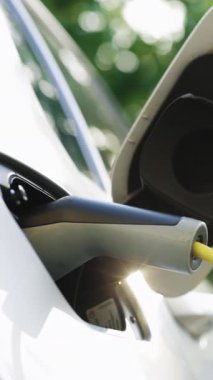 Elektrikli hibrit arabanın dikey videosu park yerindeki elektrik kablolarından şarj oluyor. Elektrikli araba yükleniyor. Araçlar yenilenebilir enerji kullanıyor. Elektrikli araç şarj oluyor.