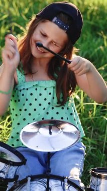 Gülümseyen, uzun saçlı, davulda çalan mutlu küçük kızın dikey videosu. Sunset 'te Davul Çalan İfade Eden Davulcu Kız. Rock Band Müzik Sanatçısı Yeni Davul Solosu Öğreniyor. El bilgisayarı görüntüsü.