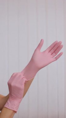 Ellerin pembe lateks eldiven giydiği dikey format videosu. Beyaz arka planda eldiven giyen bir kadının iki eli. Viral hastalıkların önlenmesi.