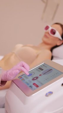 Güzellik salonunda lazer epilasyon makinesi kullanan bir kadının dikey format videosu. Estetik kliniğinde lazer tüy temizleme makinesini kontrol eden bir terapist.