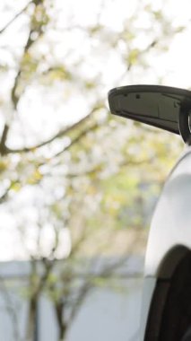 Elektrikli arabaları açan kadının dikey format videosu baltayı şarj etmek için fişe takıyor. Kadının park yerinde şarj etmek için fişe taktığı yakın çekim..