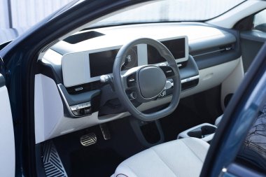 Elektrikli bir aracın direksiyonu, dahili kokpit, elektrikli düğmeler, dijital hız göstergesi, ön koltuklar, tekstil, pencereler, konsol, vites kolu. Dijital dokunmatik ekranlı araç paneli.