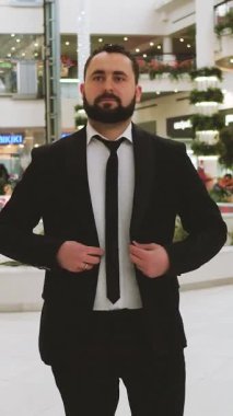 Takım elbiseli şık iş adamının dikey videosu ceketini düzeltiyor, alışveriş merkezindeki portresi. Kendine güvenen ve kararlı beyaz adam kravatını ve ceketini düzeltiyor.