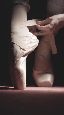 Balerin 'in dikey format videosu bale ayakkabısı giyiyor. Bale ayakkabılarını giyen bir balerin..