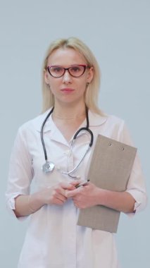 Beyaz önlüklü ve steteskoplu bir kadın doktorun beyaz arka plandaki kameraya gülümseyen portresinin dikey formatı. Konsept: doktor, sağlık hizmetleri, ilaç aşkı.