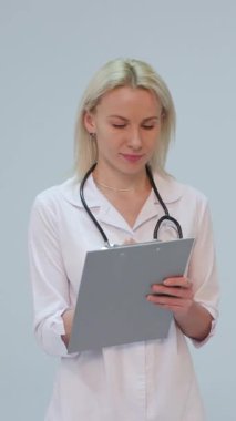 Beyaz önlüklü ve steteskoplu bir kadın doktorun beyaz arka plandaki kameraya gülümseyen portresinin dikey formatı. Konsept: doktor, sağlık hizmetleri, ilaç aşkı.