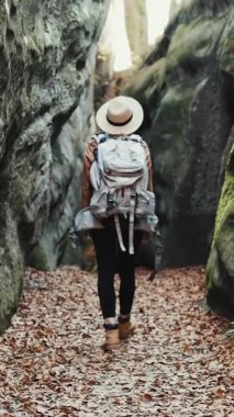 Kayalarda yürüyen genç gezgin kızın dikey görüntüsü, kayalarda yürüyen kadın turist, şehir manzarası. Şık şapkalı çekici genç bayan etrafa bakıyor..