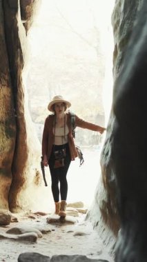 Kayaların üzerinde yürüyen genç bir kızın dikey format videosu, gezgin bir kadının orman yürüyüşü, şehir manzarası. Güneşli bir günde dağda yürüyen bir kadın yürüyüşçü.