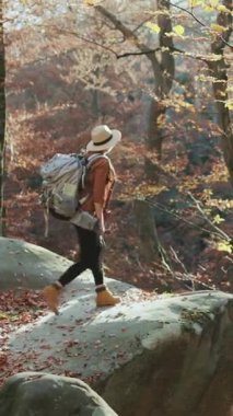 Genç ilham veren kadının dikey videosu güzel gündoğumu gökyüzüne karşı bir dağın tepesinde ellerini kaldırıyor. Sırt çantalı ve keçeli şapkalı heyecanlı gezgin kız diyor ki: