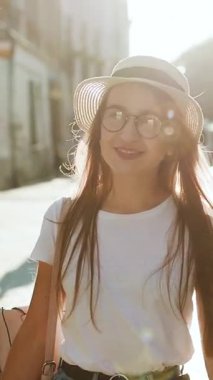 Avrupa 'da gezen ve Lviv' de güzel manzaraları keşfeden çekici genç bir kadının dikey format videosu, güneş ışığı parlaması, yavaş çekim, gözlüklü hippi kız, tatilde eğleniyor.