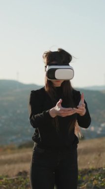 VR kulaklıklı kızın dikey videosu macera oyunu, gençlik eğlencesi, aktivite. Gelecek şu andır. VR konsepti. Fütürist VR kulaklık takan bir kadın. Sanal gerçeklik kulaklığı kullanan kadın.