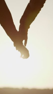 Birbirine Bağlı İki Aşığın Dikey Videosu. Günbatımı Arkaplanı 'nda el ele tutuşan Kadın ve Adamın Silueti' ni detaylandır. Çift Güven, Aşk ve Mutluluk konsepti. Gerçek aşk, ortaklık, aşk hedefleri.