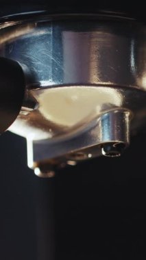 Profesyonel makineden kahve dökülürken çekilmiş dikey bir video. Barista adam filtre tutacağı kullanarak duble espresso yapıyor. Taze kahve akıyor. Sabahları sade kahve içmek.