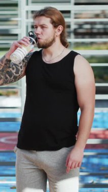 Susamış adamın vücut geliştirme eğitimi sırasında şişeden spor kokteyli içtiği dikey format videosu. Spor antrenmanından sonra spordan su içen yorgun bir sporcu..